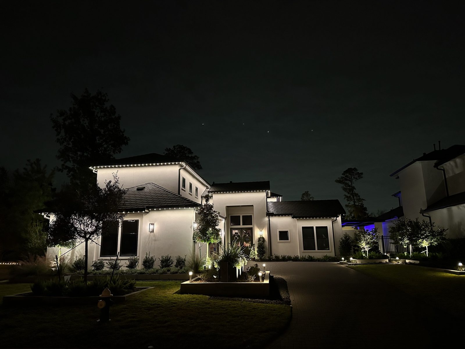 Warm white permanent roofline lighting outlining the eaves of a modern white San Antonio home