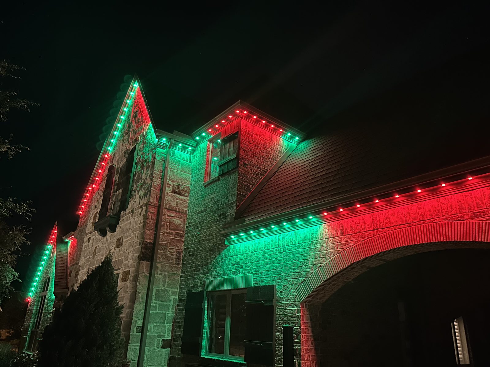 Permanent roofline lighting on a stone home displaying red and green holiday colors