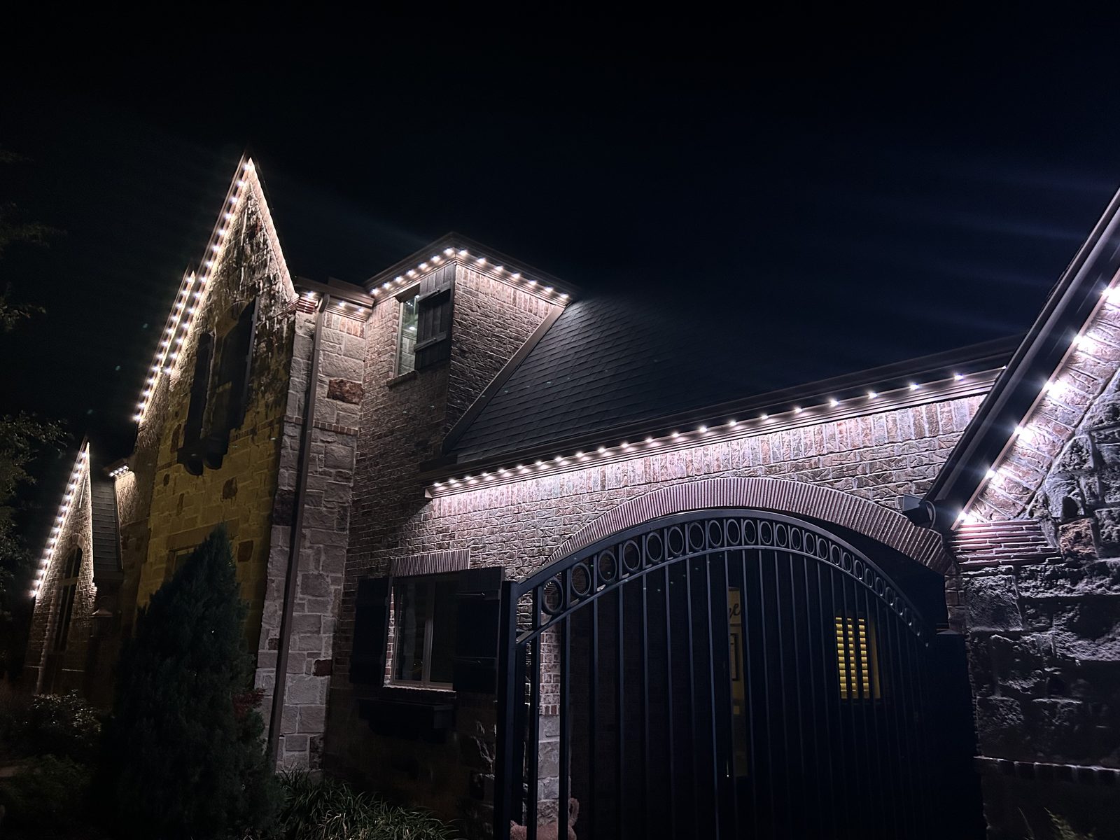 Warm white permanent roofline lighting on a two-story stone home at night